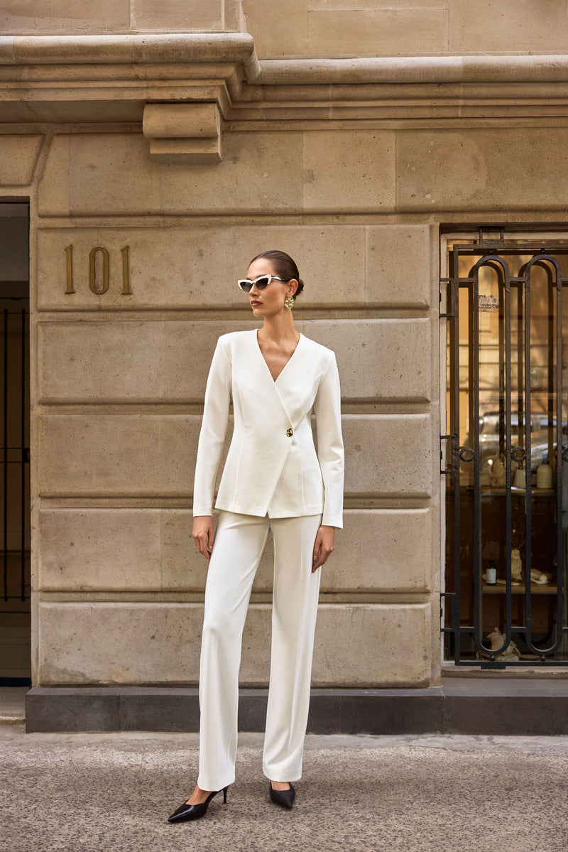 Weißer Zweiteiler mit Sonnenbrille – stilvoller City-Look mit klaren Linien vor klassischer Steinwand